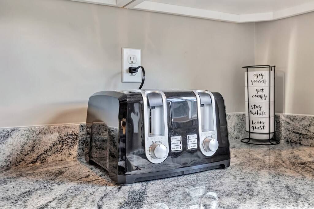 A black toaster on a granite countertop with a power outlet and a motivational sign in the background.