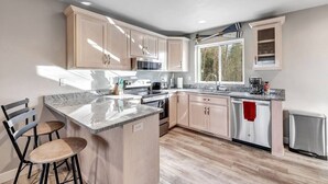 A modern kitchen with light wood cabinets, a granite countertop, stainless steel appliances, and a large window providing natural light. - CONDO 5-Sister Bay Gem-Steps to the Beach (Sister Bay)