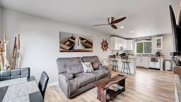 A modern living room with a grey sofa, wooden coffee table, and a dining area with a black table and grey placemats.