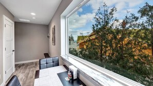 A modern dining area with a large window, a table set for two, and a view of a building and trees outside. - CONDO 5-Sister Bay Gem-Steps to the Beach (Sister Bay)