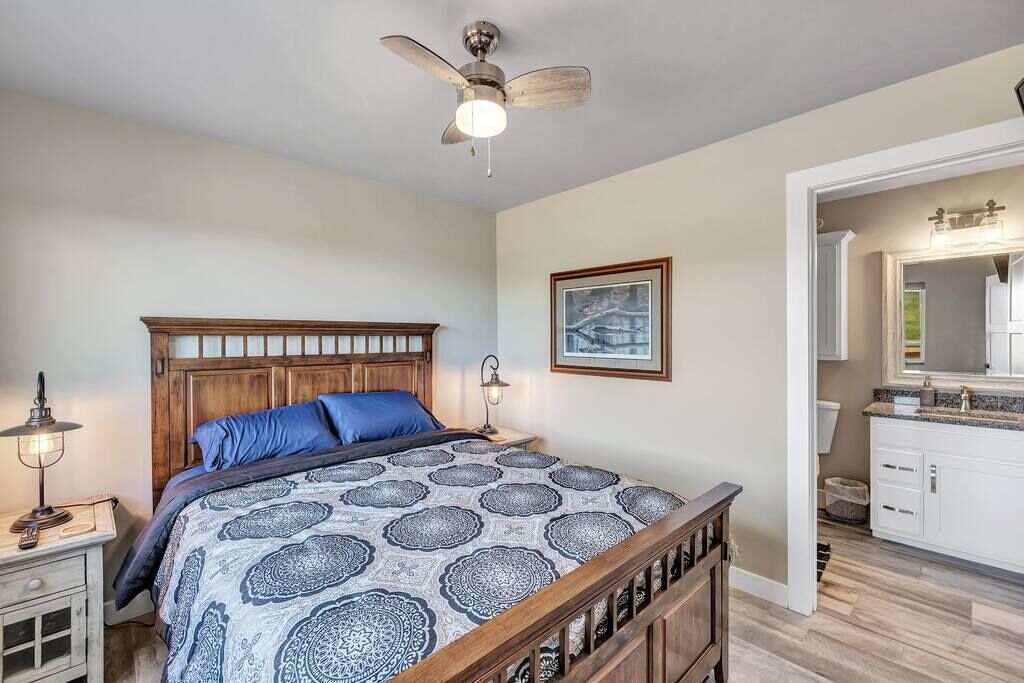A bedroom with a wooden bed, a ceiling fan, a nightstand with a lamp, and a framed picture on the wall.