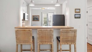 A kitchen with a wooden island, three wicker chairs, pendant lighting, and a refrigerator. - Downtown 2nd Floor Apartment with Dramatic Lake Views.   (Petoskey)