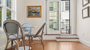 A dining area with wicker chairs and a table, a painting on the wall, and a view through a glass door. - Downtown 2nd Floor Apartment with Dramatic Lake Views.   (Petoskey)