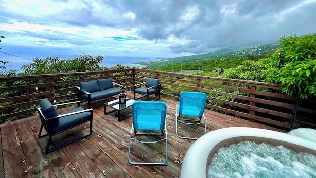 A wooden deck with outdoor seating and a hot tub, overlooking a lush landscape and the ocean. - Romantic villa with whirlpool bath 5mns from the beach! (Saint-Leu)