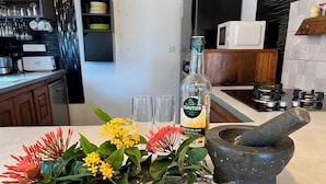 A kitchen counter with a bottle of Isautier, two glasses, a mortar and pestle, and a bouquet of flowers. - Romantic villa with whirlpool bath 5mns from the beach! (Saint-Leu)