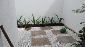 A small garden area with white pebbles and stepping stones, surrounded by green plants and a yellow watering can.