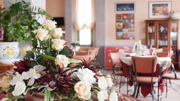 Une salle à manger avec des tables dressées, une grande composition florale au premier plan et une vue sur la salle à manger en arrière-plan.