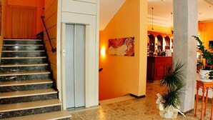 Un hall d’hôtel avec un escalier en marbre, une moquette rouge, un grand tableau et un coin bar.