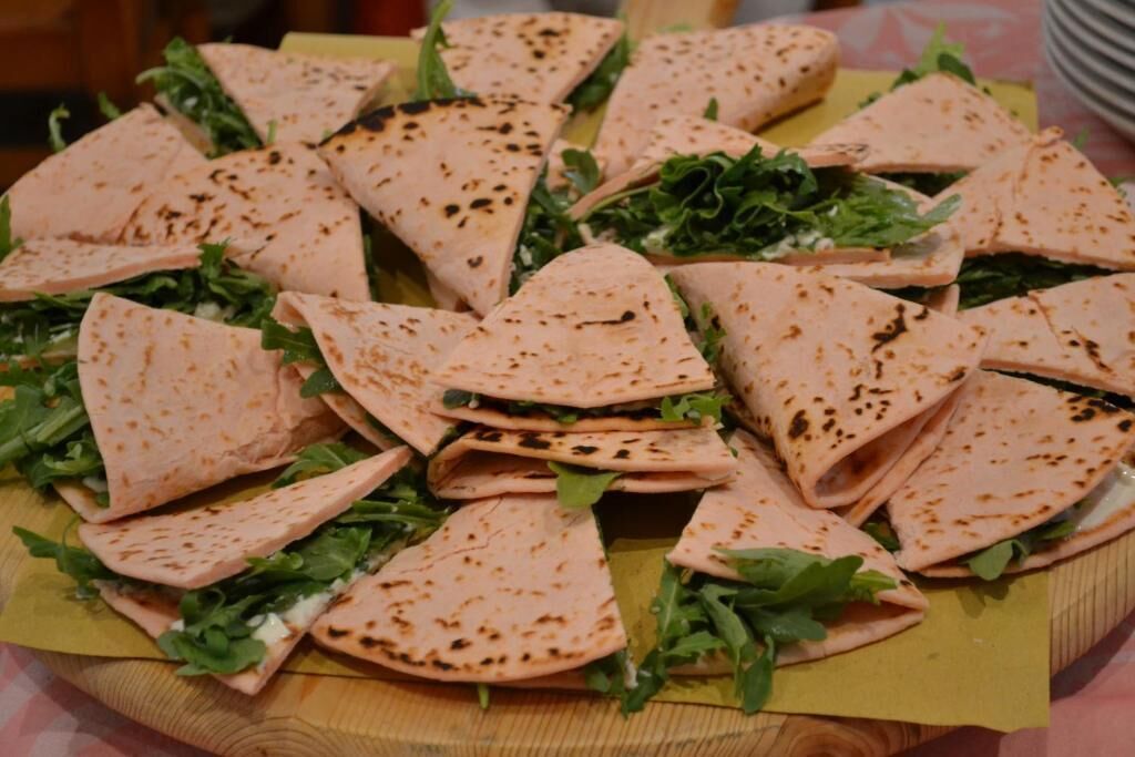 Une table en bois sur laquelle on trouve une assiette de pains plats pliés, certains garnis, et des légumes frais.