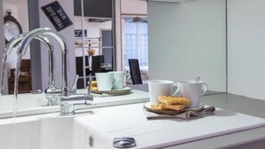 Une salle de bain moderne avec un lavabo blanc, un miroir et un robinet. On y trouve deux tasses blanches et une assiette avec un biscuit posé sur le comptoir.
