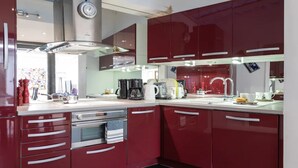 Une cuisine moderne avec des meubles rouges, des appareils en acier inoxydable et une horloge bien visible au mur.