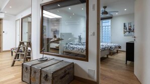 Une chambre avec un grand miroir, une commode en bois, un lit avec une literie à motifs et un ventilateur de plafond.