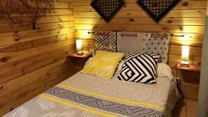 Una habitación de cabaña de madera con una cama, dos mesitas de noche y paneles decorativos en la pared.