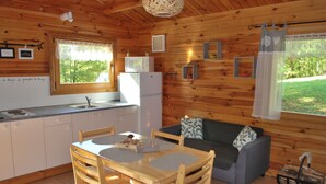 Una cabaña de madera con cocina y comedor, que incluye un refrigerador, microondas y una mesa de madera con sillas.