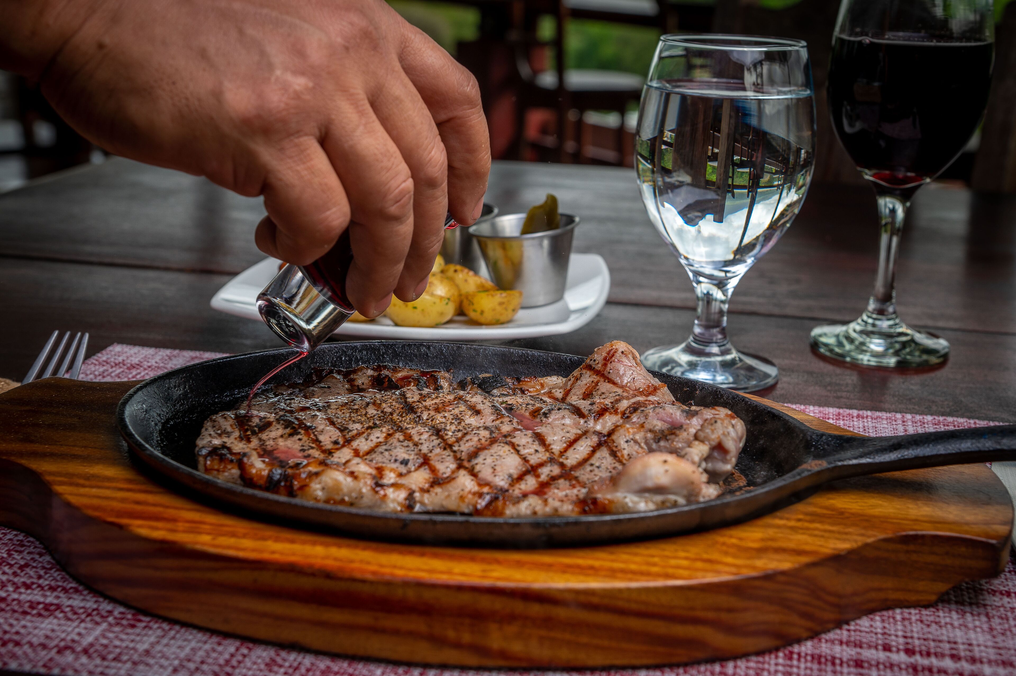 Egy rácsra helyezett, grillezett steak, egy pohár víz és egy pohár vörösbor az asztalon.