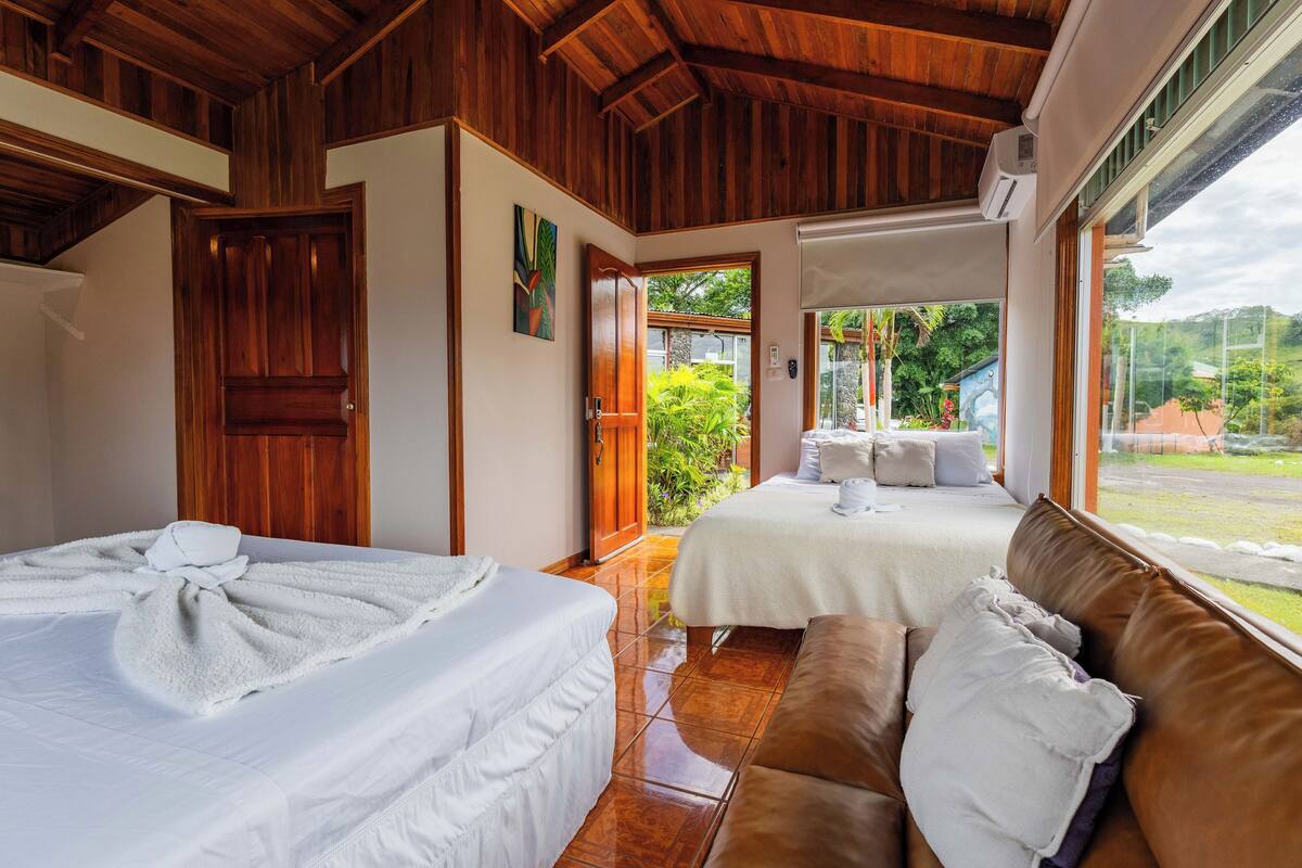 A hotel room with two beds, a wooden ceiling, and a view of the garden.