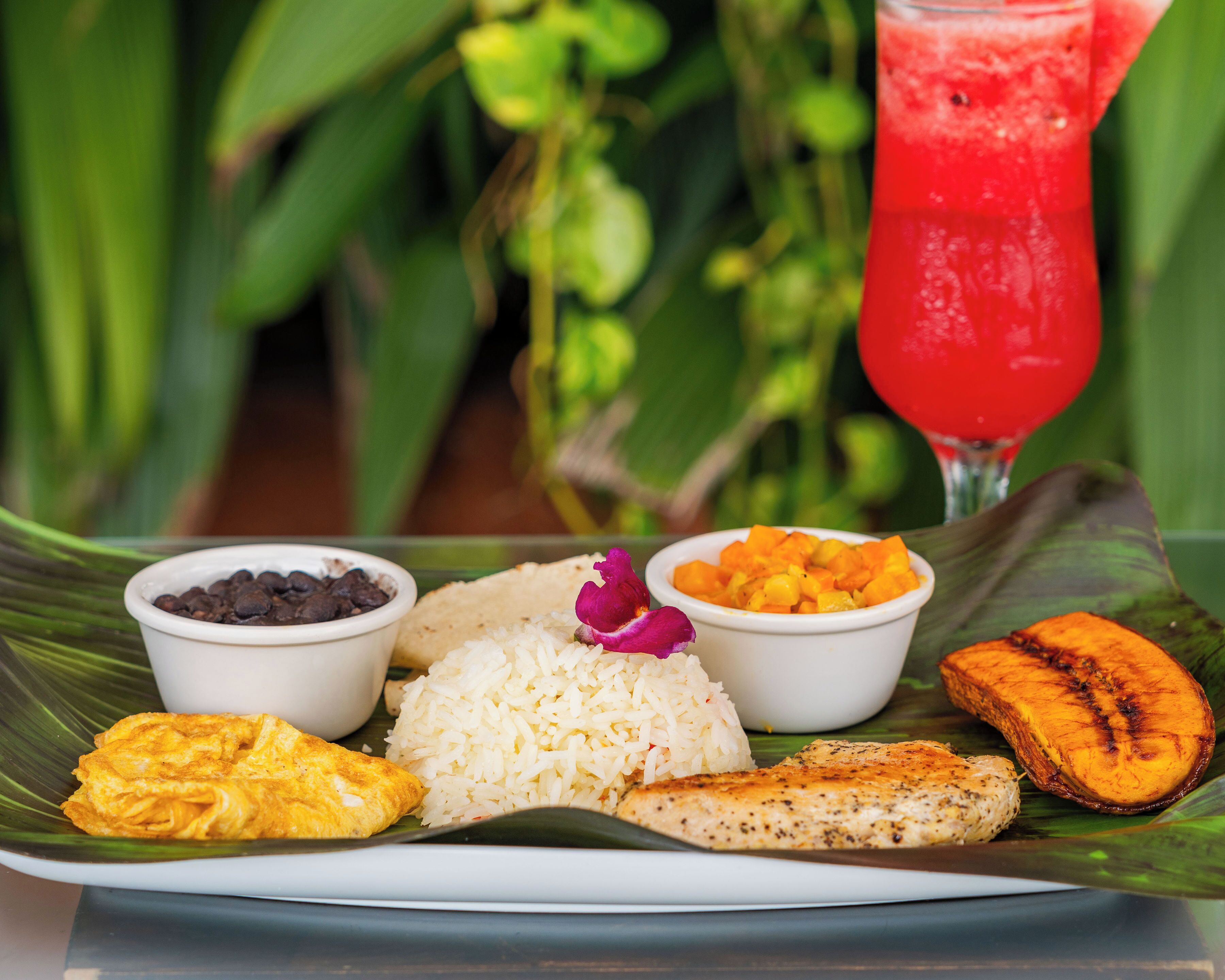 Plato de comida con arroz, frijoles, un pedazo de pollo frito y una rebanada de plátano sobre una hoja de plátano.