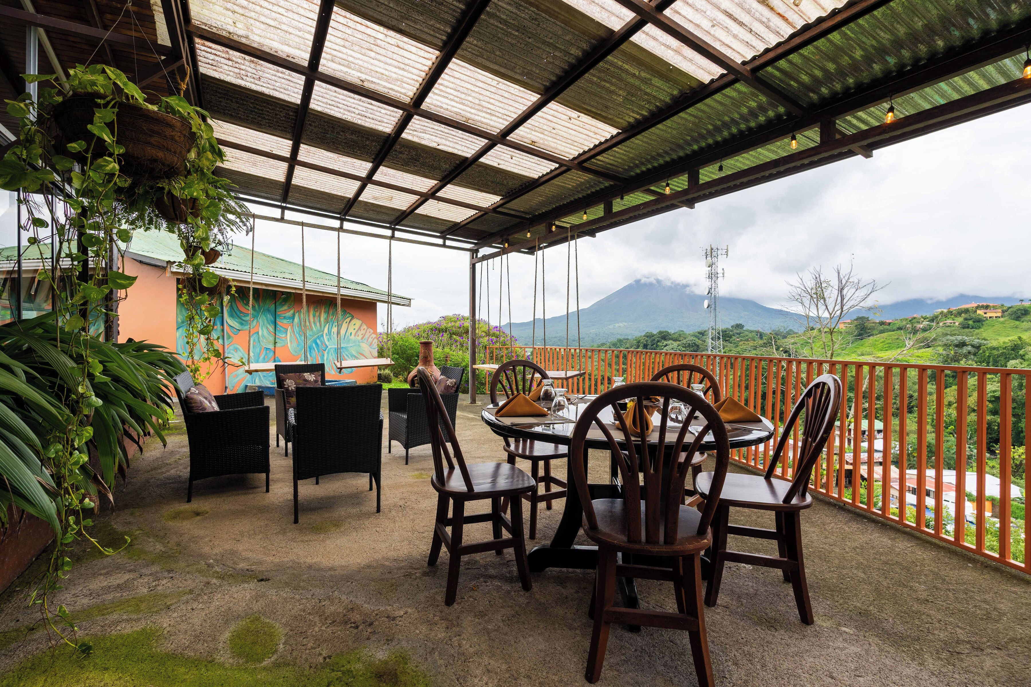A covered outdoor seating area with chairs and tables, overlooking a mountainous landscape.