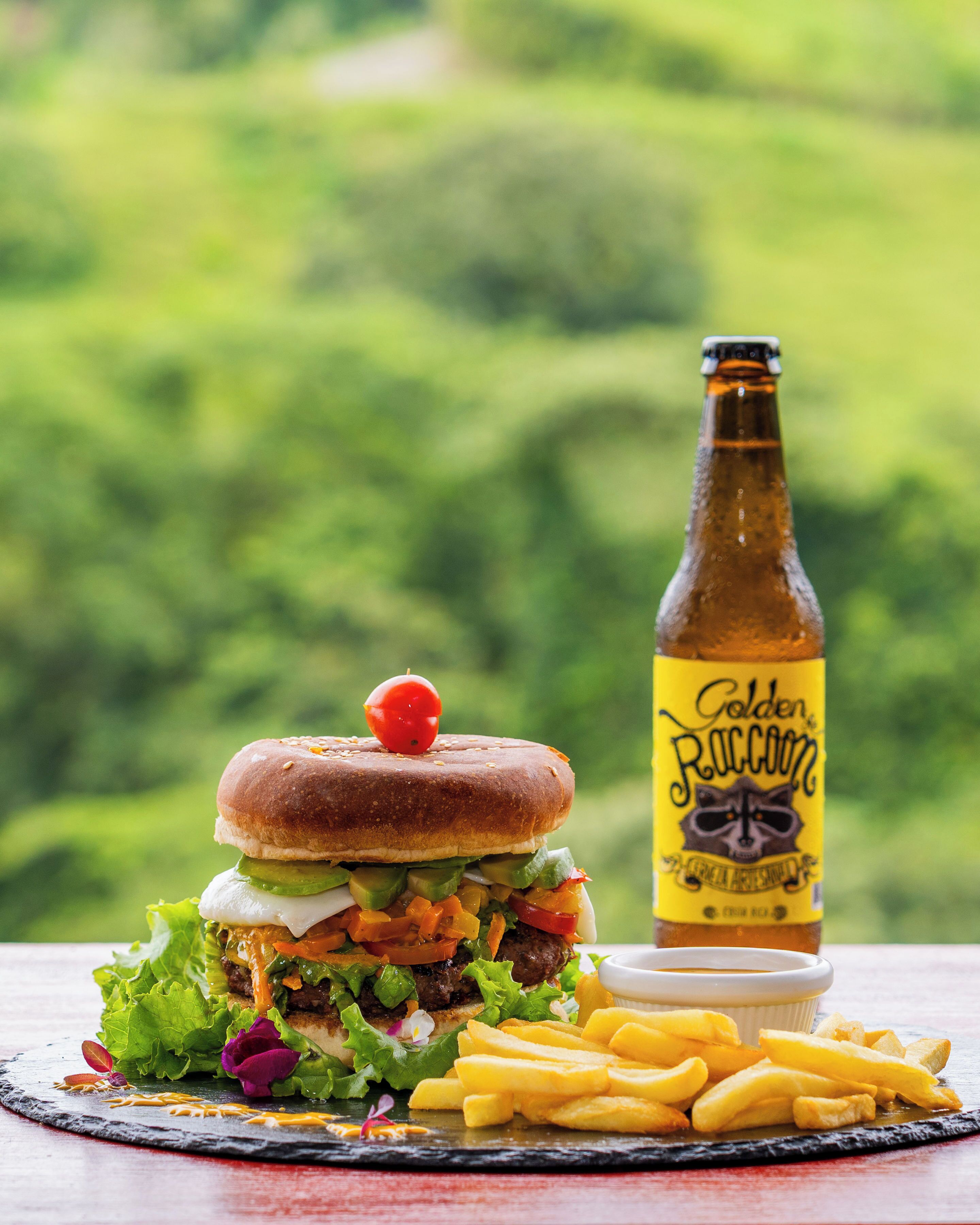 A burger with fries and a bottle of beer on a table with a green background.