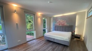 A modern bedroom with a large bed, sliding glass doors, and a view of greenery outside. - Schmuckstück traumhafter ehem. Bahnhof in Alleinlage (Braunfels)