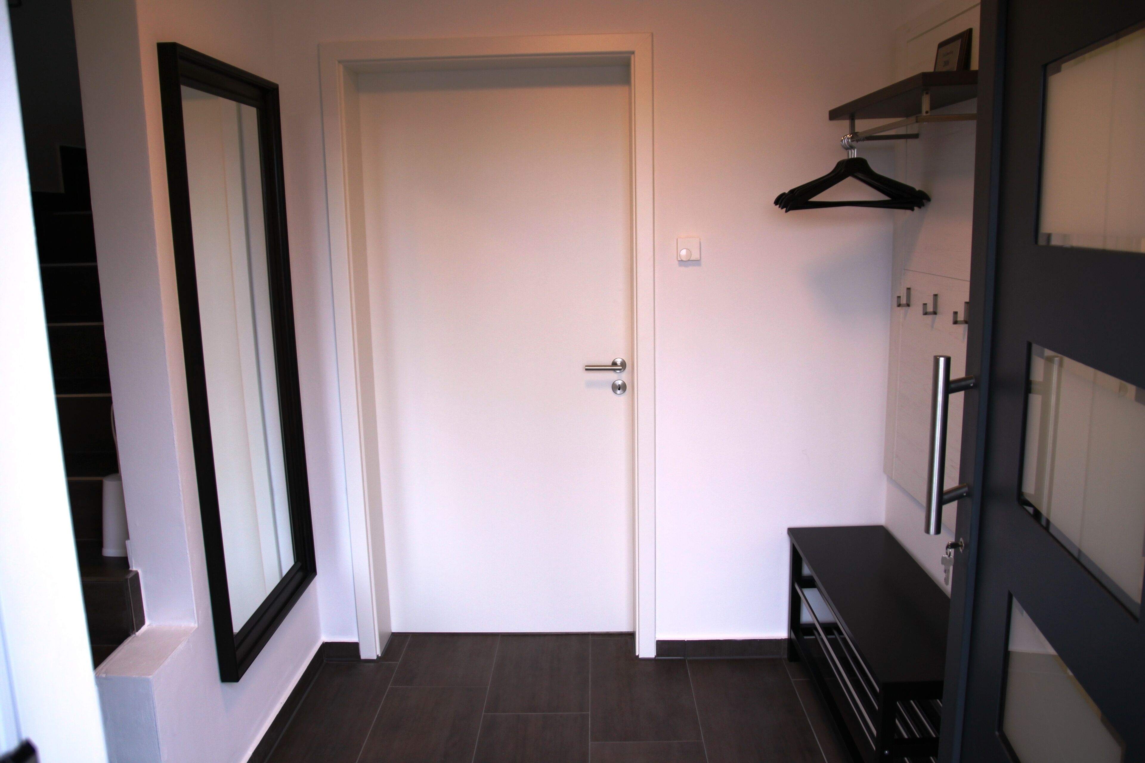 A hallway with a white door, a coat rack, and a black bench.