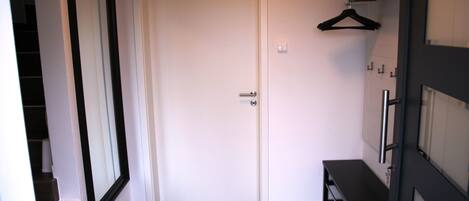 A hallway with a white door, a coat rack, and a black bench.