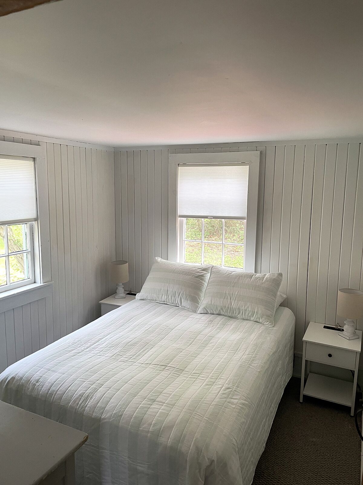 Ein Schlafzimmer mit einem großen Bett, zwei Nachttischen und zwei Fenstern mit Jalousien.