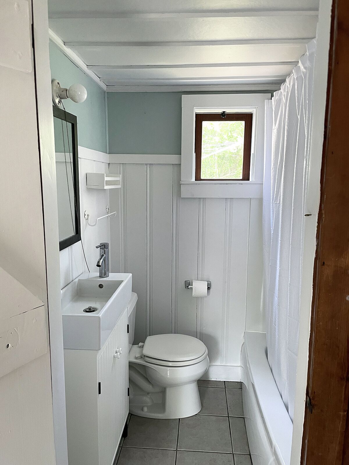 A compact bathroom with a toilet, sink, and a small window above the toilet.