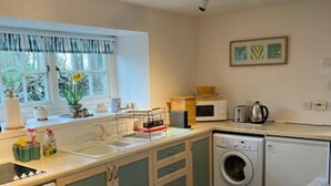 A compact kitchen with a sink, stove, microwave, and washing machine. - Stable Cottage -  spacious one level cottage with private courtyard. (Berwick-upon-Tweed)