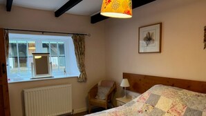 A bedroom with a large bed, a chair, a window with curtains, a radiator, and a wall-mounted lamp. - Stable Cottage -  spacious one level cottage with private courtyard. (Berwick-upon-Tweed)