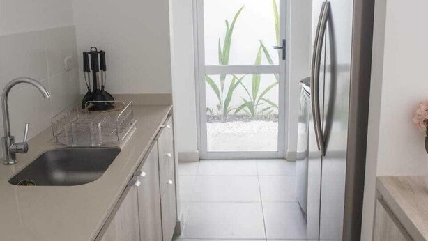 A modern kitchen with a sink, stainless steel refrigerator, and a view to a balcony.
