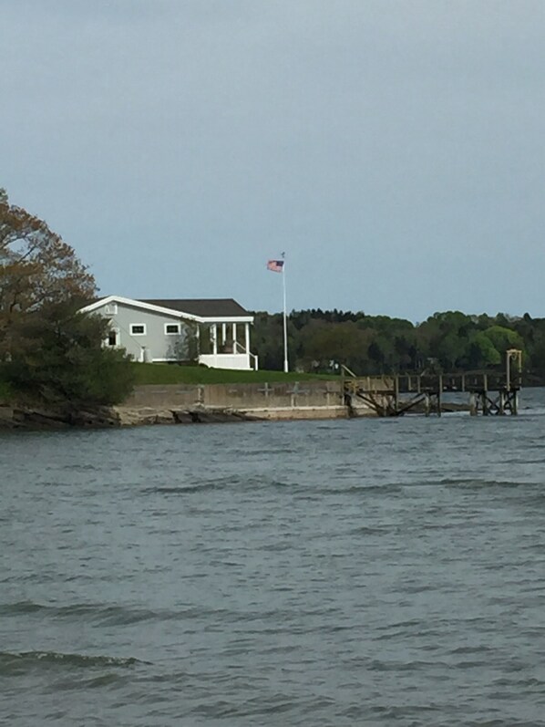 Une maison située au bord d’un plan d’eau, avec un mât pour drapeau.