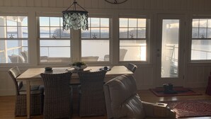 Un comedor con mesa y sillas, ventanas amplias con decoraciones de estrellas de mar y vista al agua.
