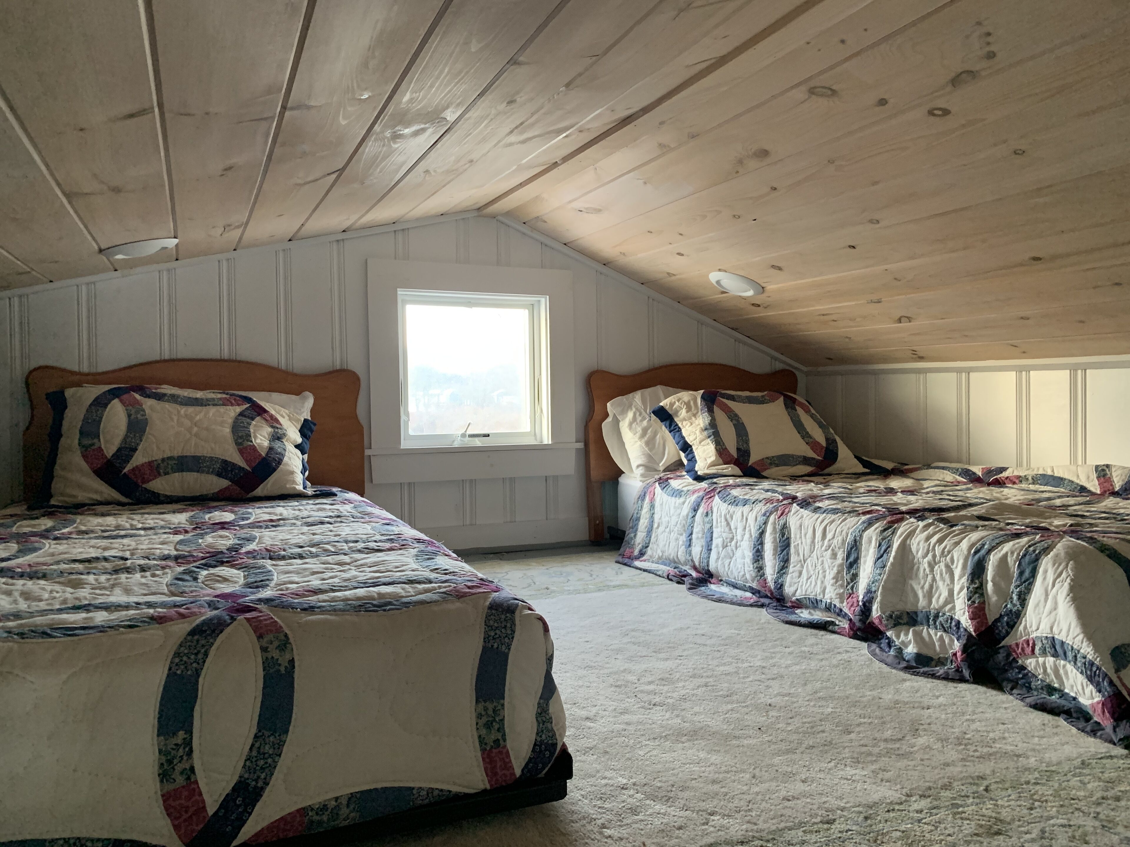 Een slaapkamer met twee bedden, houten balken in het plafond, een raam en uitzicht op de omgeving.