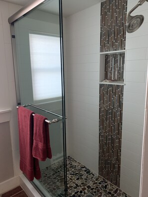 Une douche entièrementClose avec des parois en verre, un sol carrelé et un mur décoré d’une mosaïque verticale.