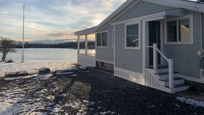 Una casa con porche cubierto, una escalera y vista a un lago.