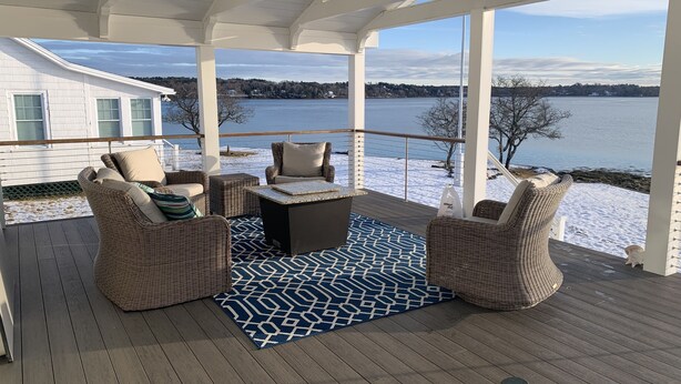 Una terraza cubierta al aire libre con mobiliario de mimbre, un tapete estampado y vistas a un lago y edificios lejanos.
