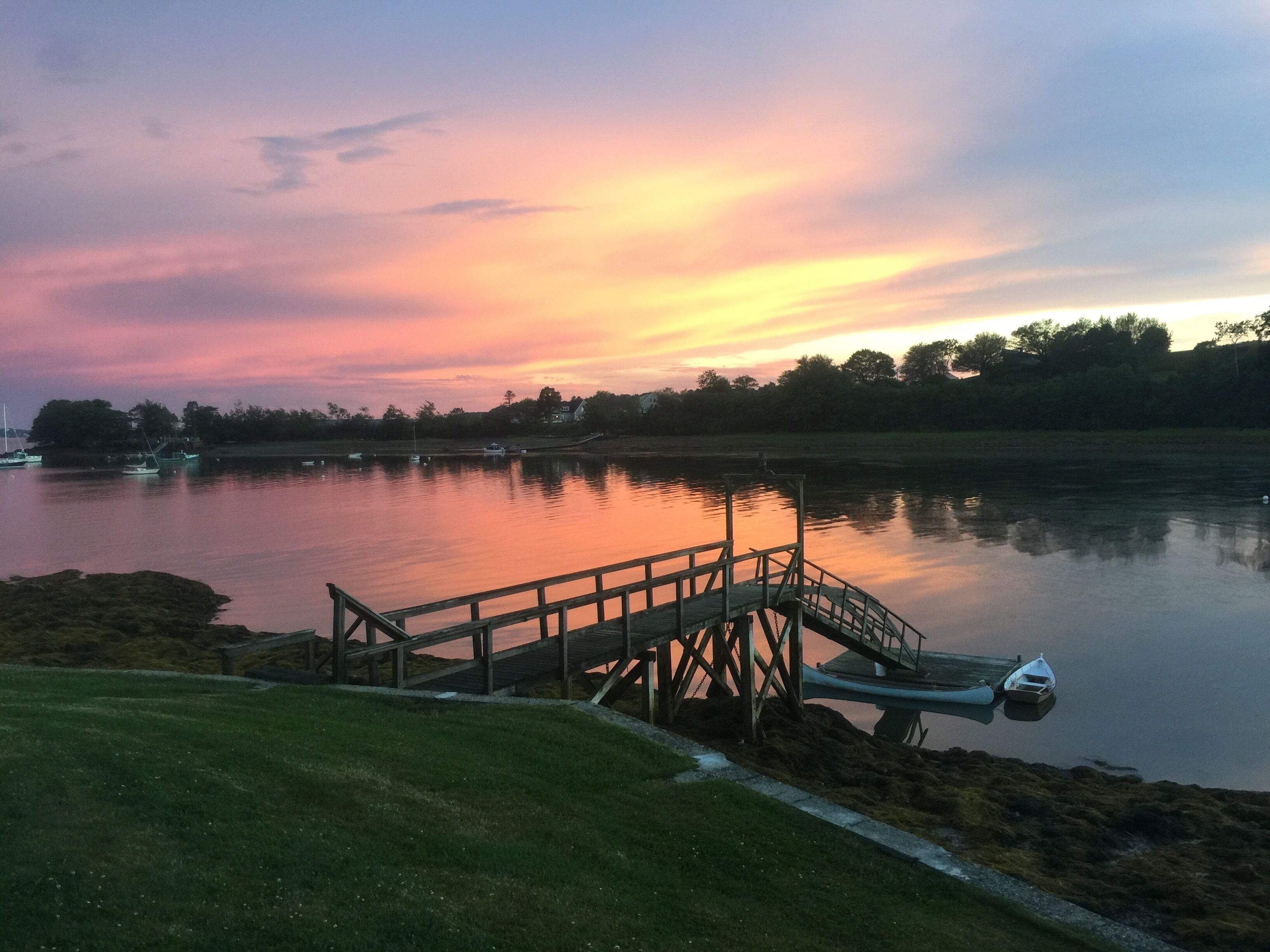 Une jetée en bois s’étendant sur une étendue d’eau calme, avec un coucher de soleil en arrière-plan.