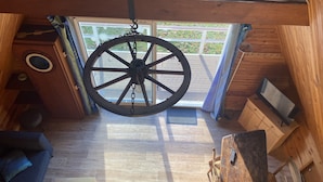 A wooden interior with a large wheel hanging from the ceiling, a wooden floor, a sofa, and a small table.