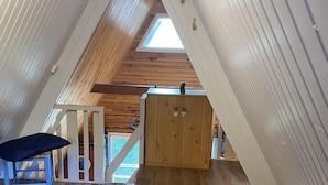 A loft bedroom with a wooden floor, a bed, a chair, and a wardrobe.