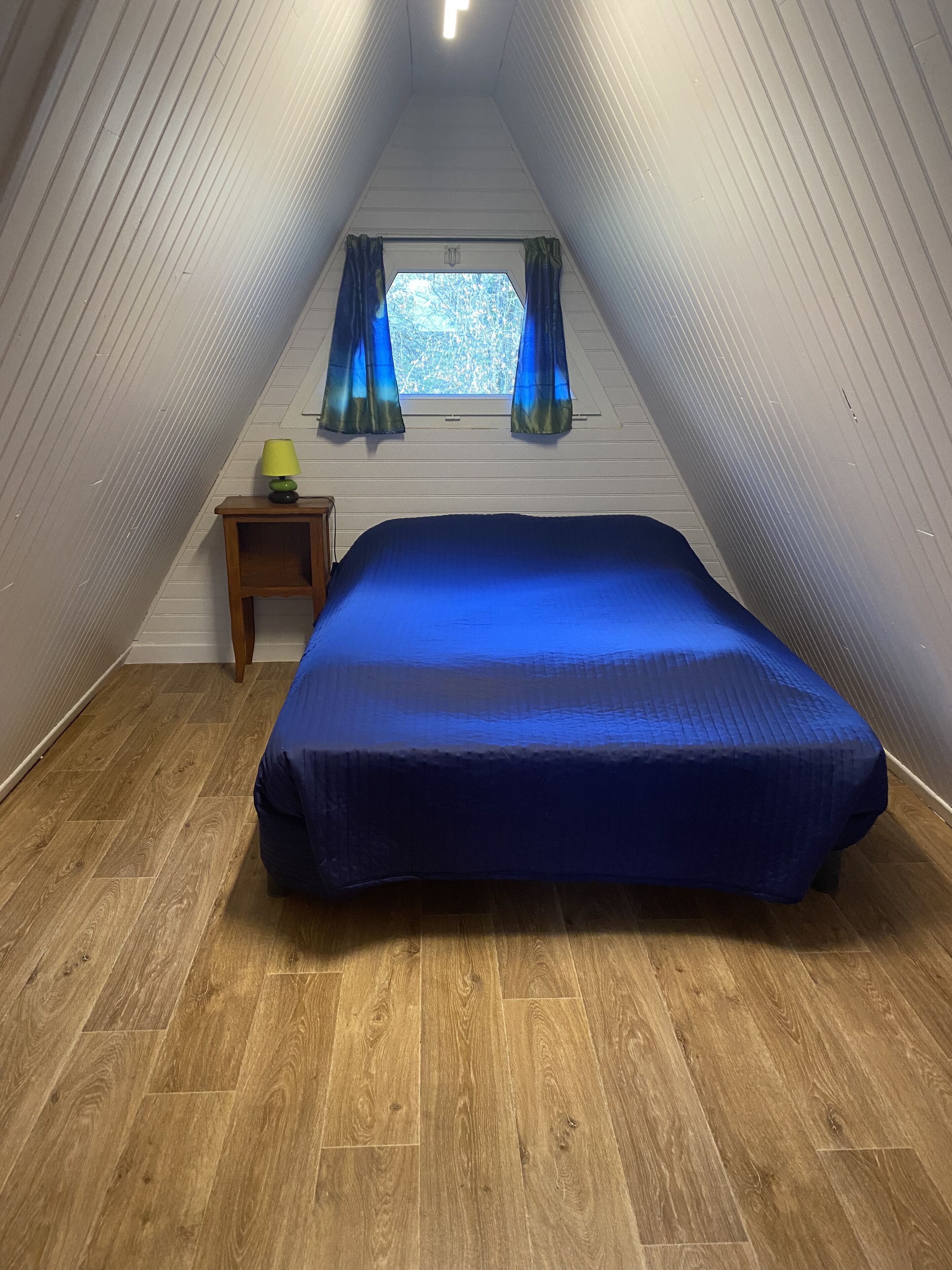A bedroom with a bed, a small table, a lamp, and a window with curtains.