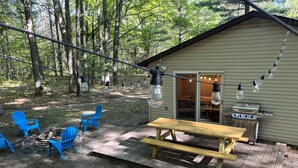 A cabin with a wooden deck, a picnic table, and blue Adirondack chairs.