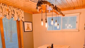 A wooden dining table with benches, a chandelier, and a window with blinds.