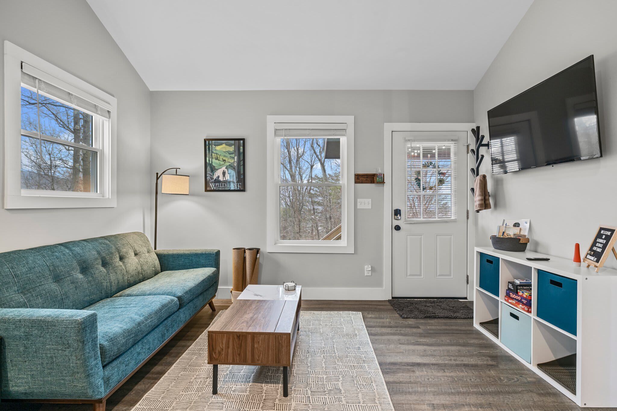 Un salon moderne avec un canapé de couleur turquoise, une table basse en bois et un téléviseur fixé au mur.