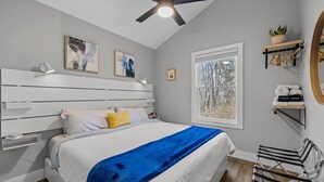 A bedroom with a bed, a ceiling fan, a window, and a bedside table.