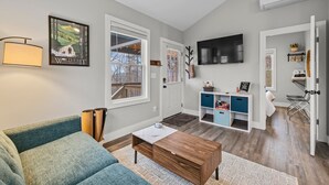 A modern living room with a sofa, coffee table, and TV. There is a door leading to a laundry area with a drying rack.