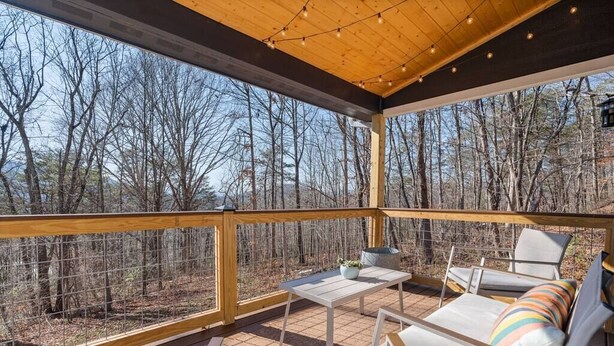 A covered outdoor deck with a wooden railing, a table, and two chairs.
