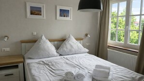 A neatly made bed with white linens, two pillows, and rolled towels on a wooden nightstand. - Bright apartment with direct access to the garden (Sankt Peter-Ording)