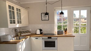 A kitchen with white cabinetry, a wooden countertop, a toaster, a coffee maker, and a window with a view of greenery. - Bright apartment with direct access to the garden (Sankt Peter-Ording)