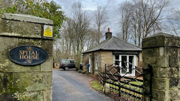 Una puerta de piedra con un letrero que dice "Spital House" que da acceso a un pequeño edificio de piedra con techo a dos aguas.